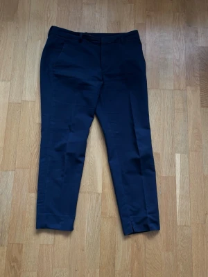 Mörkblå kostymbyxor från Zara Woman - Snygga mörkblå kostymbyxor från Zara Woman med raka ben och diskreta fickor i sidan. Byxorna har hällor för skärp och är tillverkade i ett mjukt, vävt material som ger en stilren look. Perfekta för dig som gillar klassisk och enkel stil.