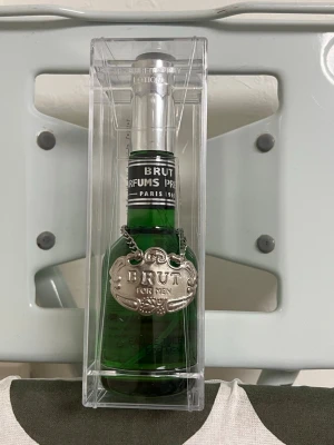 Brut parfym för män 100 ml - Klassisk parfym från Brut för män i en grön glasflaska med silverfärgat lock och en dekorativ metallbricka runt halsen. Flaskan rymmer 100 ml och kommer i en genomskinlig plastförpackning. En ikonisk doft med vintagekänsla.