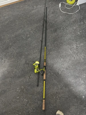 Gul fiskespö med rulle - Säljer ett tvådelat fiskespö med gul och svart design samt korkhandtag. Spöt har en matchande gul fiskerulle med lina monterad. Perfekt för dig som vill komma igång med fiske eller behöver ett extra spö till samlingen.