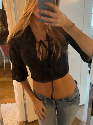 Svart vintage blus med snörning - svart croppad blus med trekvartsärm och snygg snörning framtill som man kan knuta lite hur man vill. broderade detaljer och v-ringad halsringning. Från vintage label ”motivi” och köpt i Paris💞