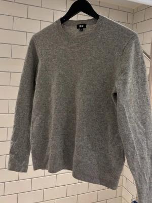 Grå Kashmir tröja från Uniqlo - Säljer en stilren grå kashmir tröja från Uniqlo. Tröjan är i mjukt material och har en klassisk passform som funkar till det mesta. Passar folk upp till 170cm