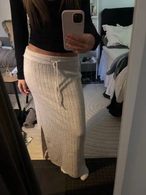 Beige ribbad långkjol med snörning - Mysig beige långkjol med ribbad struktur och snörning i midjan. Kjolen har en rak passform och är perfekt för en avslappnad men ändå stilren look. Tillverkad i ett mjukt stickat material som känns skönt mot huden. Jag är 158 och den är perfekt i längden på mig, då jag vill ha den lågmidjad!