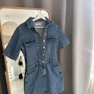 Kort jeansklänning från Zara - Säljer en kort jeansklänning med korta ärmar, krage och knappar framtill. Superfin blå färg som passar till sommaren!!