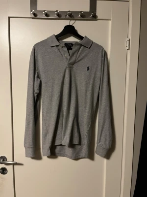 Grå långärmad piké från Ralph Lauren - Snygg långärmad grå piké från märket ralph lauren. Knappt använd!