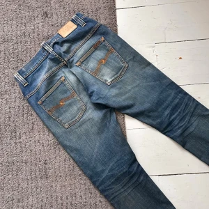 Mörkblåa Nudie Tape Ted Jeans - Riktigt snygga Nudie jeans med en vintage look & sjuka fades. | W29 L32. | Riktigt fint skick, inga hål el slitningar förutom näst intill osynliga slitningar vid cuffsen längst ner. | Längd: 97, Midja: 39-42cm (Stretch). | Sjuka honeycombs och fina fades. | Pris ej hugget i sten, skriv vid minsta fundering!