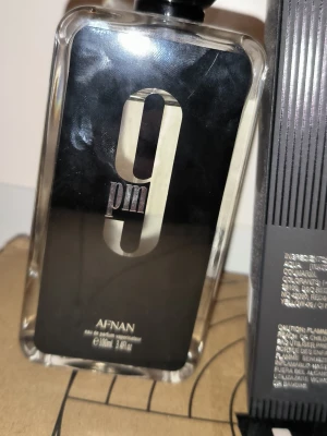Afnan 9pm Eau de Parfum - Afnan 9pm Eau de Parfum är en elegant parfym i en svart och transparent glasflaska med en stor svart rund kork. Flaskan har en modern design med silverdetaljer och kommer i en matchande svart, räfflad kartong. Den är nästan helt full. Priset är ej hugget i sten.