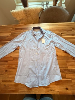Ljusblå skjorta från Bruun & Stengade - Helt ny ljusblå skjorta från Bruun & Stengade i slim fit. Skjortan har klassisk krage, långa ärmar och knappar framtill. Tillverkad i bomull och enkel att ta hand om 