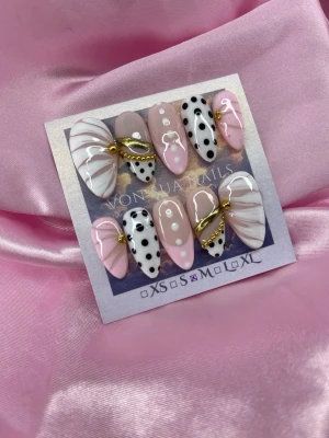 Bijou (M);Medium Almond - Snygga handgjorda press-on naglar i en medium mandelform. Mix av rosa, vitt och svart med swirl-mönster, prickar och guldfärgade kedjedetaljer. Naglarna har en glansig finish och cool design som sticker ut. Perfekt för dig som vill ha unika och trendiga naglar.M: 16 mm, 12 mm, 12,5 mm, 11,5 mm, 10 mm