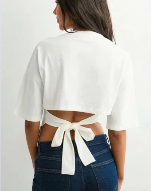 Vit knyt tröja - Säljer en vit topp med korta ärmar och snygg knytning i ryggen. Toppen har en öppen rygg och är perfekt för festtillfällen men också vardag. Trendig och lätt att matcha! Endast använd 2 ggr och inga tecken på användning. 