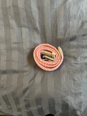 Rosa flätat bälte - Snyggt flätat bälte i rosa och beige med silverfärgat spänne. Bältet har detaljer i mocka vid spännet. Bältet är ca 90 cm 