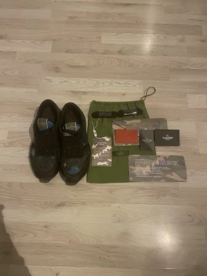 Valentino camo sneakers i svart och blå - Snygga sneakers från Valentino med svart och blått camo-mönster. Skorna har svarta snören, robust sula och detaljer i läder och textil. Märkeslogga på plösen och insidan. Perfekta för dig som vill sticka ut med exklusiva sneakers  väldigt slitna och sulan på sidan är trasig 