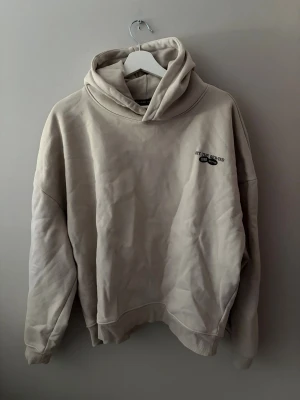 Beige hoodie med tryck från 198 Button - Säljer en beige oversized hoodie från 198 Button med try BT 'HIT THE REWIND' på ryggen och mindre logga på bröstet. Hoodien har stor huva och ribbade muddar vid ärmar och nederkant. Perfekt för en avslappnad och trendig look.