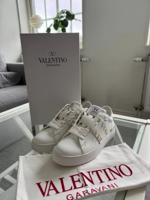 Vita Valentino Garavani sneakers - Ett par vita Valentino Garavani-sneakers med snygga guldfärgade nitar längs sidorna. 