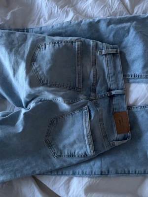 Ljusblå bootcut jeans från Pull&Bear - Säljer ett par ljusblå jeans från gina tricot med bootcut-modell och höga fickor bak. Jeansen har klassisk femficksdesign, normalhög midja och är tillverkade i mjuk denim. Perfekta för en avslappnad och trendig look.