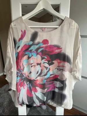 Blommig blus från Phase Eight - Säljer en luftig blus från Phase Eight i storlek M. Blusen är beige med ett stort färgstarkt blommönster i rosa, turkos, svart och vitt. Den har rund halsringning och trekvartsärmar. Perfekt för dig som gillar unika prints och en avslappnad stil.