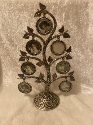 Vintage släktträd i metall - Säljer ett dekorativt släktträd i silverfärgad metall med sex runda fotoramar. Trädet har detaljerade blad och en mönstrad fot. Perfekt som personlig inredning eller present. Ramarna är av metall och har ett antikt utseende.