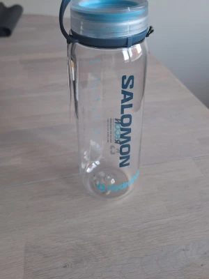 Helt ny Salomon vattenflaska 750ml - Vattenflaska från Salomon, modell Recon Twist & Sip, rymmer 750 ml. Flaskan är tillverkad av 50% återvunnen plast och har ett blått lock med bärhandtag. Perfekt för träning, vandring eller vardagsbruk.
