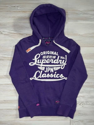 Lila Superdry hoodie med tryck - Säljer en lila hoodie från Superdry med stort vitt tryck på bröstet där det står 'Superdry JPN Classics'🤩 Storlek S och är i fint skick🙌🏻 Hör av er vid snabbaffärer samt funderingar😇