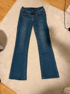 Blå bootcut jeans med fickor - Snygga blå bootcut jeans med klassiska fem fickor och kontrastsömmar. Storlek 38 regular.  Jeansen har en låg midja och är tillverkade i ett mjukt denimtyg som ger en bekväm passform. Byxorna är från madlady och bara använt fåtal gånger då de är för långa för mig. 💕