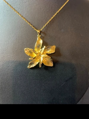 Guldigt halsband med blomma - Snyggt halsband med en stor, detaljerad blomma som hänge i guldfärgad metall. Kedjan är tunn och elegant, och blomman har en cool, organisk form med tydliga ådringaror på kronbladen. Perfekt för dig som vill sticka ut med ett unikt smycke.