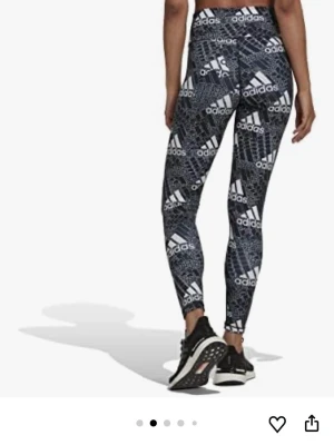 Svarta Adidas leggings med logga - Snygga svarta leggings från Adidas med vit logotyp och grafiskt mönster över hela plagget. Hög midja och tight passform som sitter skönt. Perfekta för träning eller chill. Tillverkade i stretchigt material som ger bra rörelsefrihet.