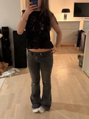 Svart spettopp med volangdetaljer - Snyggt svart spetstopp med volangdetaljer längs axlarna och hög hals. Toppen är ärmlös och har ett feminint blommigt spetsmönster som ger en trendig och elegant look. Perfekt att styla med jeans eller kjol för en cool outfit. Skriv för mer info och bilder💕💕