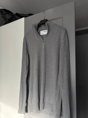 Grå zip-tröja från Selected Homme - Säljer en stilren grå tröja från Selected Homme med halvzip och hög krage. Perfekt för lager-på-lager och enkel att matcha med jeans eller chinos. Materialet är mjukt och bekvämt, och tröjan har långa ärmar och diskret design.