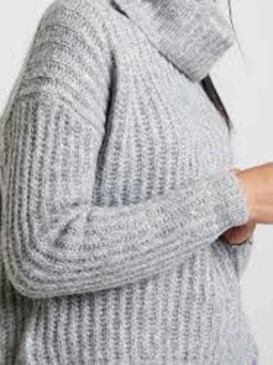 Ljusgrå stickad polotröja - Mysig ljusgrå stickad polotröja med bred ribbstickning och hög krage. Tröjan har lång ärm och avslappnad passform, perfekt för kalla dagar. Materialet ser ut att vara en mjuk ull- eller ullmix som håller dig varm hela vintern.