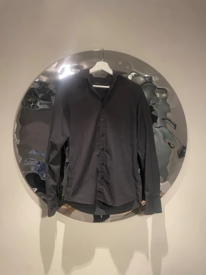 Svart skjorta med knappar - Stilren svart skjorta med klassisk krage och knäppning framtill. Skjortan har lång ärm och en rak passform som funkar till många olika looks. Tillverkad i ett mjukt tyg som känns bekvämt mot huden. Perfekt för dig som gillar minimalistisk stil.