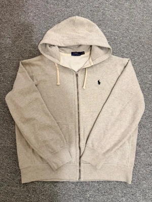 Grå Zip-up Polo Ralph Lauren - Snygg grå/beige hoodie med dragkedja från Polo Ralph Lauren. Hör av dig vid eventuella frågor och behov av fler bilder!🤗