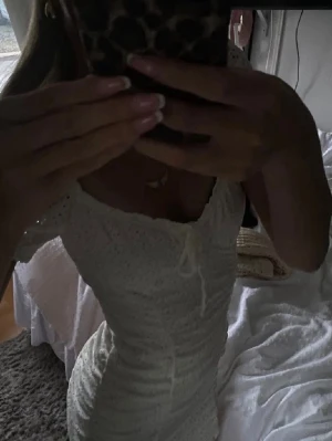 Vit spetsklänning från H&M Divided - Söt vit kortklänning från H&M Divided med spetsdetaljer och knyt framtill. Klänningen har korta ärmar och figurnära passform, perfekt för sommarens alla tillfällen. Tillverkad i bomull för en luftig och bekväm känsla.