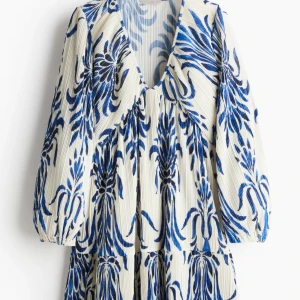  klänning - Superfin klänning med blått blommönster på vit botten. Klänningen har v-ringning, långa ärmar med resår vid ärmslut och ett luftigt fall💕