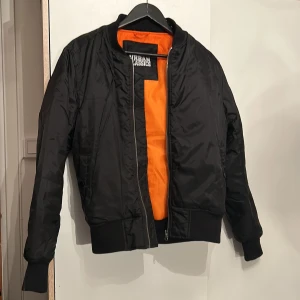 Svart bomberjacka - Urban Classics svart bomberjacka, orange innanför, i bra skick. Storlek S.