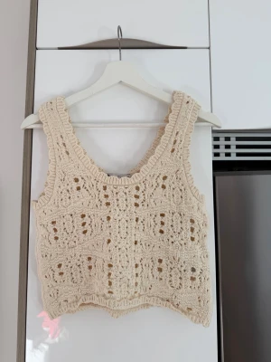 Beige virkad croppad linnetopp - Säljer en beige virkad linnetopp med breda axelband och snyggt mönster. Toppen är croppad och har en bohemisk känsla, perfekt för varma dagar. Materialet är troligtvis bomull och den är ärmlös med dekorativa virkade detaljer.