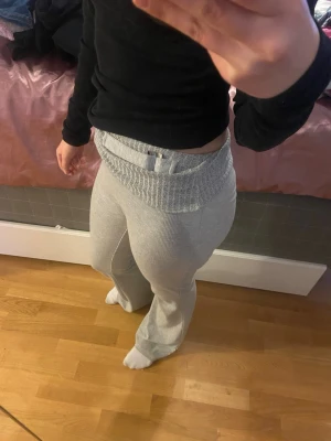 Grishgrå ribbade flare yoga byxor  - Säljer ett par grå ribbade soplounge-mjukisbyxor med bred resår i midjan och utsvängda ben. Byxorna är i mjukt stickat material och har en relaxed sopstil. Perfekta för chill dagar hemma eller när du vill grassera runt i något bekvämt.
