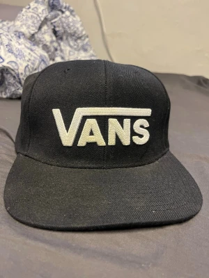 Svart snapback keps från Vans - Snygg svart keps från Vans med stor vit broderad logga framtill. Klassisk platt skärm och justerbar baksida för perfekt passform. Perfekt accessoar för en streetwear look.💕