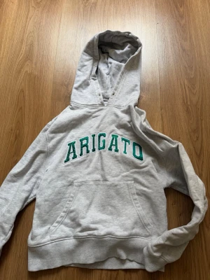 Grå hoodie från Axel Arigato - Snygg grå hoodie från Axel Arigato med grön text på bröstet. Storlek XS men lite mindre i storlek