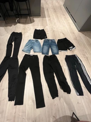 Svarta och blå jeans & byxor mix - Säljer ett gäng byxor och jeans i olika modeller. Här finns svarta raka jeans, svarta mjukisbyxor, ett par svarta byxor med vita ränder på sidan samt två par blå jeansshorts. Perfekt för dig som vill ha variation i garderoben!