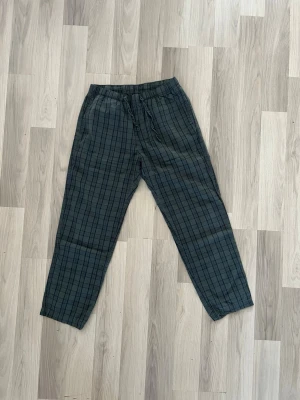 Rutiga pyjamasbyxor i grönt - Säljer ett par gråa pyjamasbyxor med svart rutmönster. Byxorna har resår i midjan och dragsko för skön passform. Perfekta för slappa dagar hemma eller mysiga kvällar. Tillverkade i mjukt tyg som känns bekvämt mot huden. Fråga mig om storlek privat.