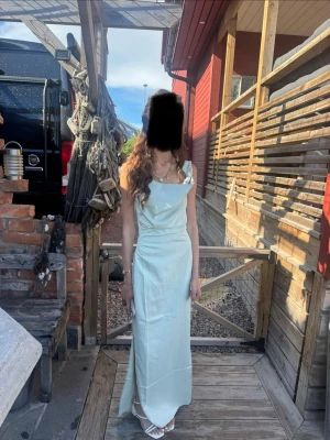 Ljusgrön adoore långklänning med slits - Snygg ljusgrön adoore långklänning med slits och axelbandslös design. Klänningen har en elegant, figurnära passform och ett mjukt, glansigt material som ger en lyxig känsla. Perfekt för speciella tillfällen, bal och studentfirande. Endast använd 1 gång vid min bal