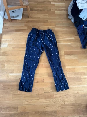 Mörkblå pyjamasbyxor Ralph Lauren - Säljer ett par mörkblå pyjamasbyxor från Ralph Lauren med vitt mönster av små loggor. Byxorna har resår i midjan och är gjorda i mjuk bomull, perfekta för chill hemma. Klassisk och avslappnad passform.