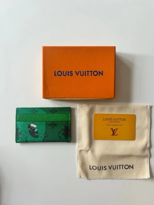 Grön Louis Vuitton card holder  - Snygg grön cardholder från Louis Vuitton med monogrammönster och svarta detaljer. Tillverkad i tåligt läder och har plats för flera kort. Kommer med original ask och dustbag. Perfekt accessoar för dig som vill ha något unikt och trendigt.