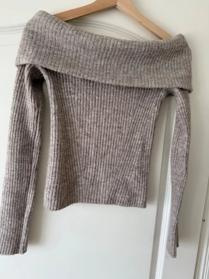 Beige off shoulder stickad tröja H&M - Säljer en beige ribbstickad off shoulder-tröja från H&M. Tröjan har bred krage som kan bäras nedanför axlarna och långa ärmar. Materialet är mjukt och stretchigt, perfekt för en trendig och avslappnad look.