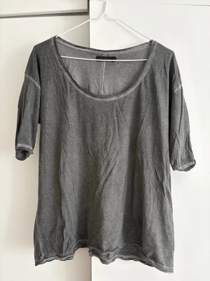 Grå t-shirt från Tiger of Sweden - En stilren grå t-shirt från Tiger of Sweden Jeans med rund halsringning och synliga sömmar. T-shirten har korta ärmar och är tillverkad i mjuk bomull, perfekt för en avslappnad look.