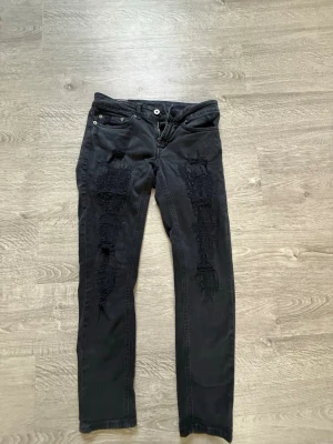 Svarta slitna dondu jeans - Säljer ett par svarta dondup jeans med  och slitningar framtill på båda benen. 