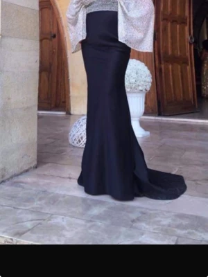Svart festklänning med figurnära passform - Elegant svart långklänning med figurnära siluett och utsvängd nederdel. Klänningen har hög midja och slät yta, vilket ger en stilren look. Perfekt för dig som vill ha en klassisk och tidlös stil. Nytt pris: 4700kr. Säljer för: 2700kr