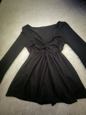 Svart långärmad topp med twist - Snygg svart långärmad topp med twistad detalj framtill och v-ringad hals. Modellen har en lätt utsvängd passform och är tillverkad i ett mjukt, stretchigt material. Perfekt för dig som gillar stilrena plagg med en liten twist.