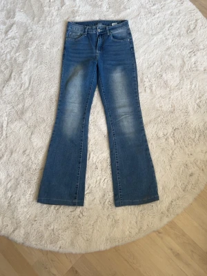 Blå bootcut jeans med broderade fickor - Ett par blå bootcut jeans med snyggt slitna detaljer och broderade bakfickor. Jeansen har klassisk femficksmodell och normal midja. Materialet är denim i bomull med lite stretch för skön passform.