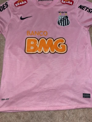 Rosa Santos FC Neymar Jr matchtröja - Säljer en rosa Santos FC matchtröja från Nike med Neymar Jr och nummer 11 på ryggen. Tröjan har flera sponsorloggor, klubbmärke på bröstet och är tillverkad i Dri-FIT material som andas. Perfekt för dig som älskar fotboll och vill sticka ut på planen.