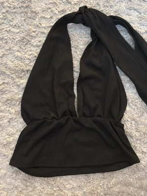 Svart ribbad halterneck topp - Säljer en svart ribbad halterneck topp. Toppen har breda band som knyts i nacken och en croppad passform. Perfekt till sommarens outfits och enkel att styla med olika accessoarer. Gåva vid köp!🎁